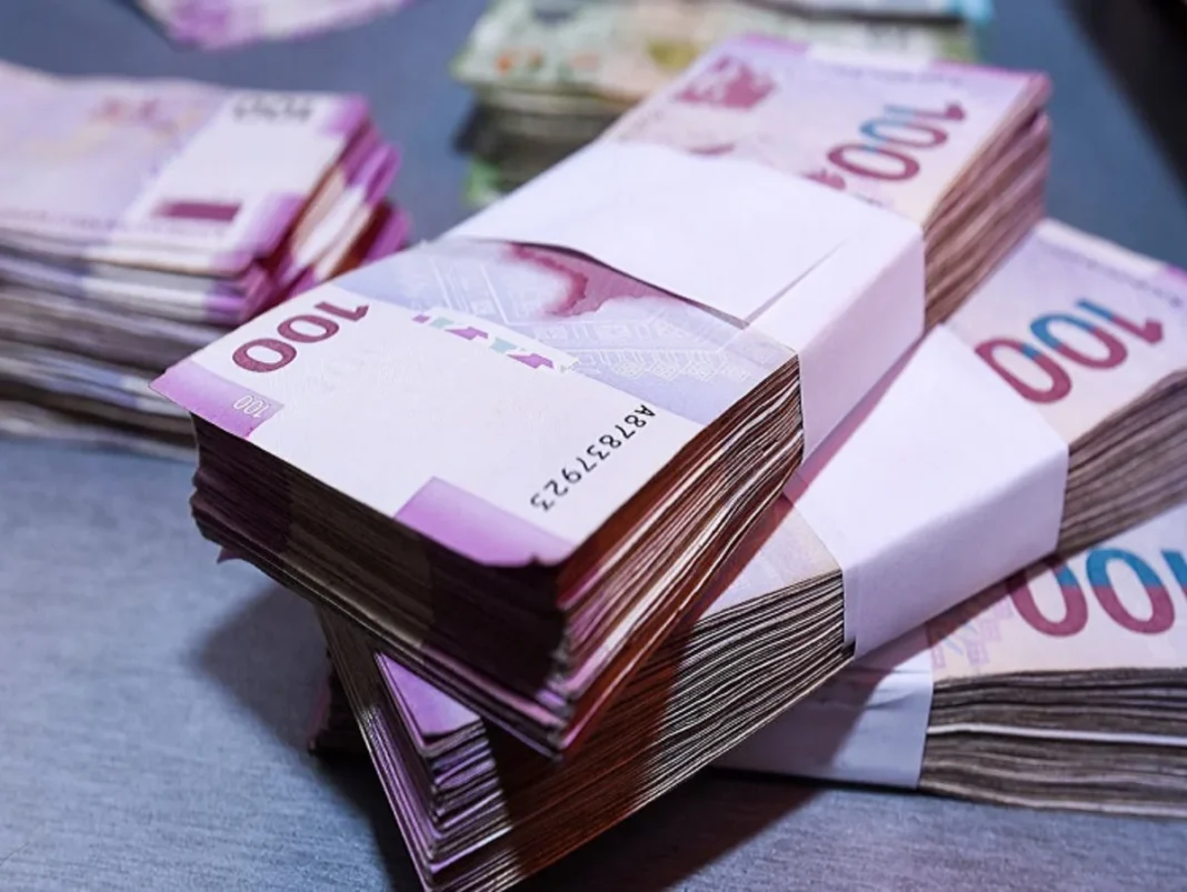 Karabağ ve Doğu Zengezur’a 2030’a kadar 13,2 milyar manat Azerbaycan bayrağı önünde manat banknotları ve madeni paralar